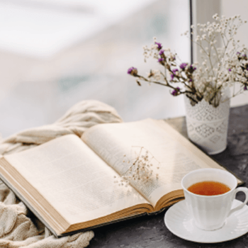 Open book, flowers and cup of tea on a desk