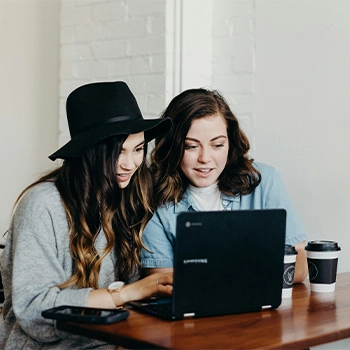 Two women looking at a laptop while drinking coffee