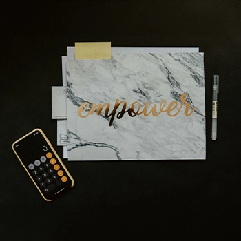 Top down photo of a mobile phone with calculator app, pen, and folder with the word 'empower' written on it.