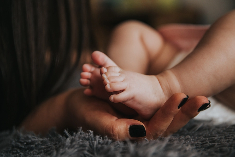 infants feet being held by a womans hand resting on a gray blanket