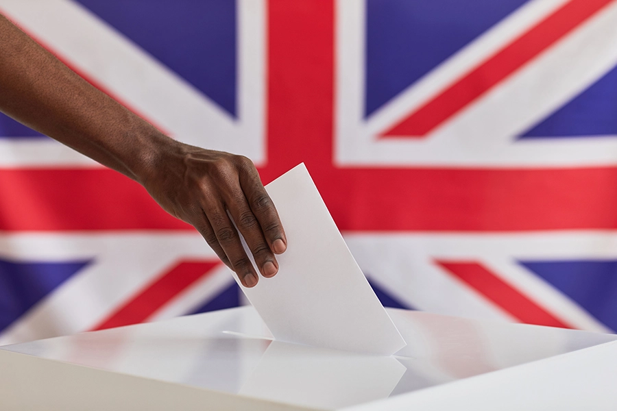 Close-up of African man putting ballot into voting box against the British flag